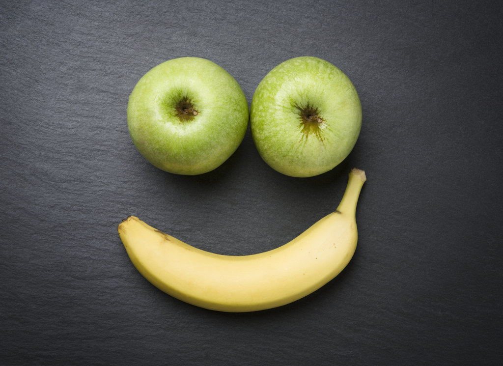 Concept "healthy is good": Smiley face with fresh apples and banana looking happy and smiling, isolated on dark grey stone plate.